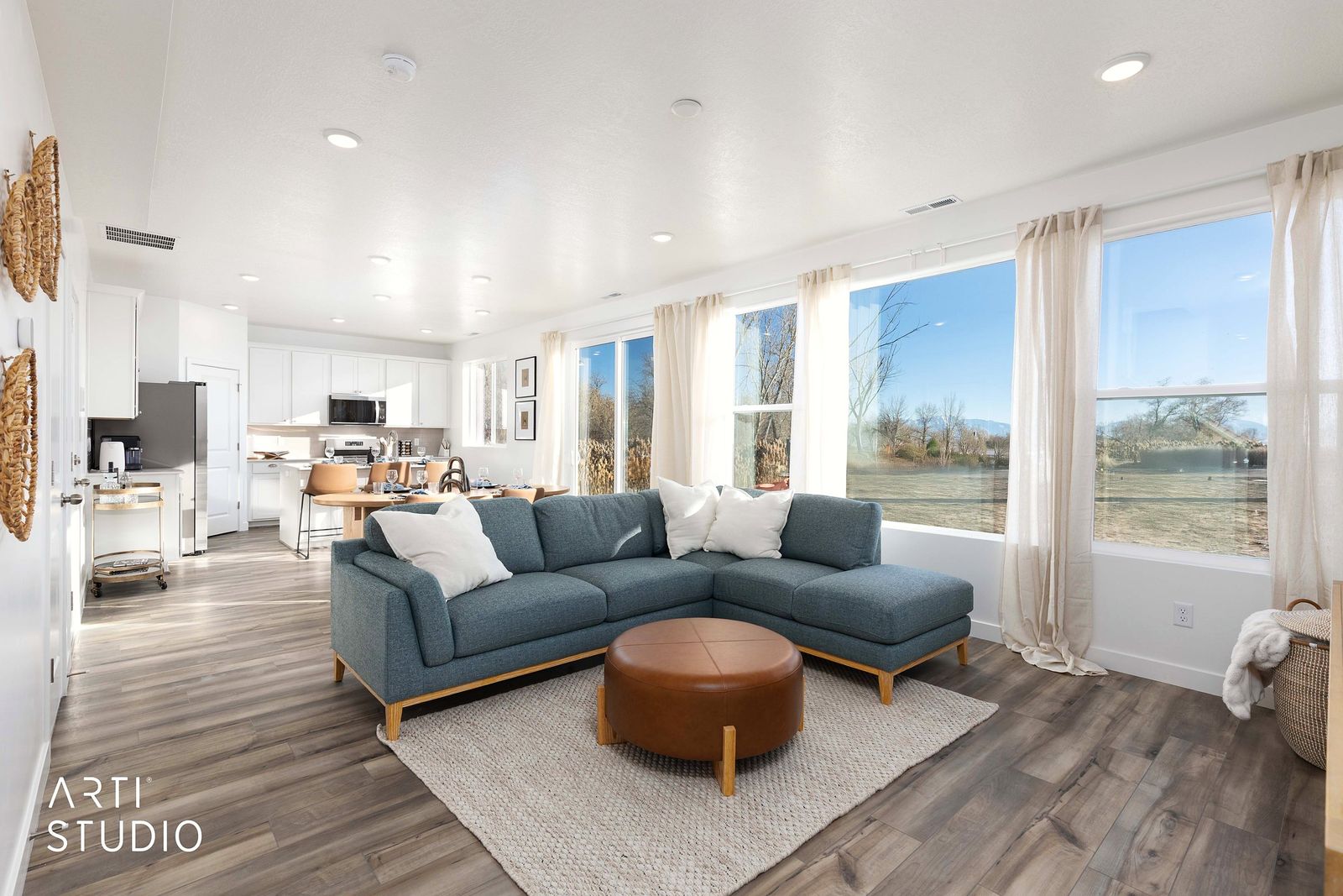 Bright living room with a blue sectional, leather ottoman and tall windows toward the lake