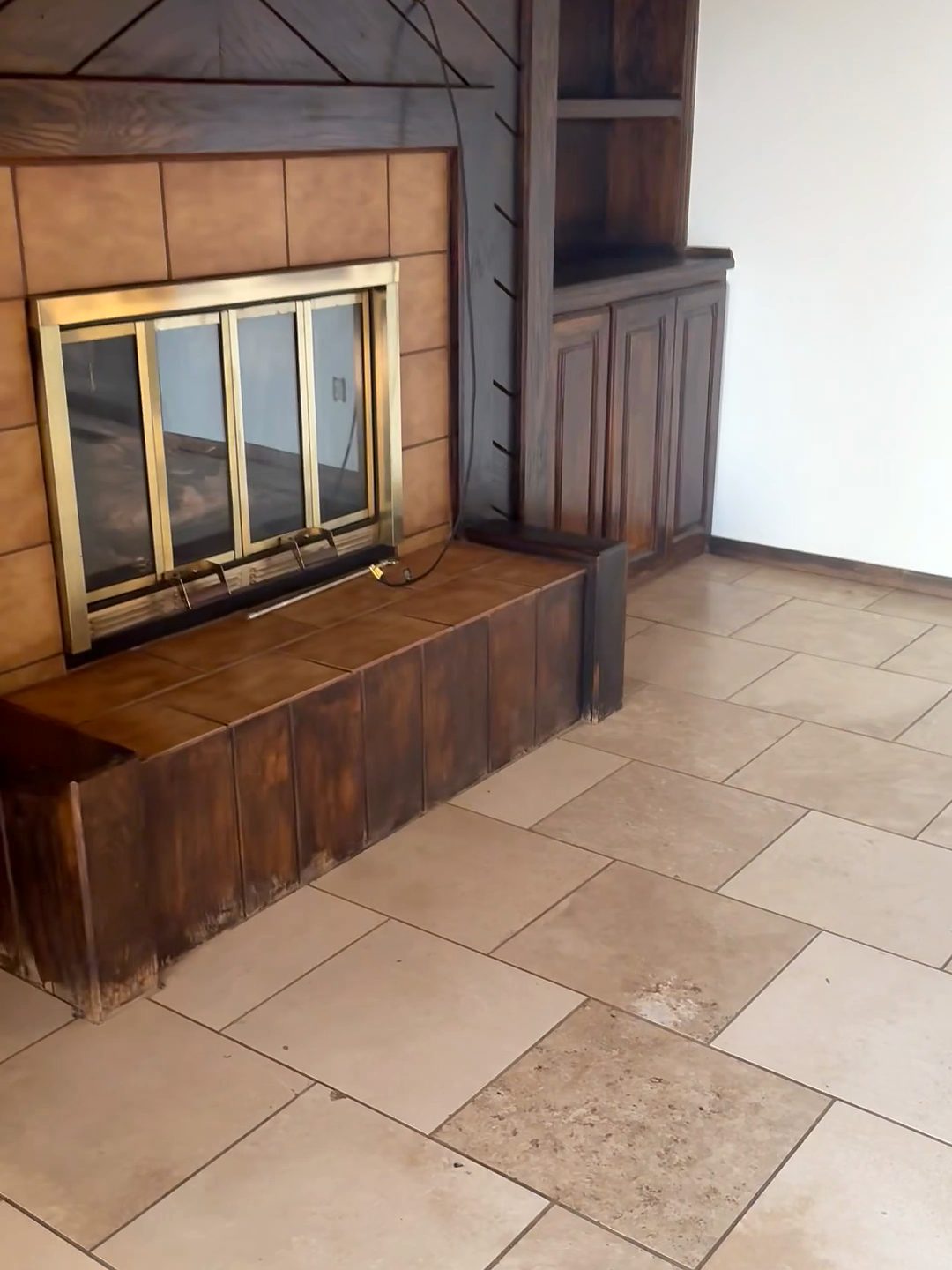 Original fireplace with a brass surround, brown tile and dark wood paneling