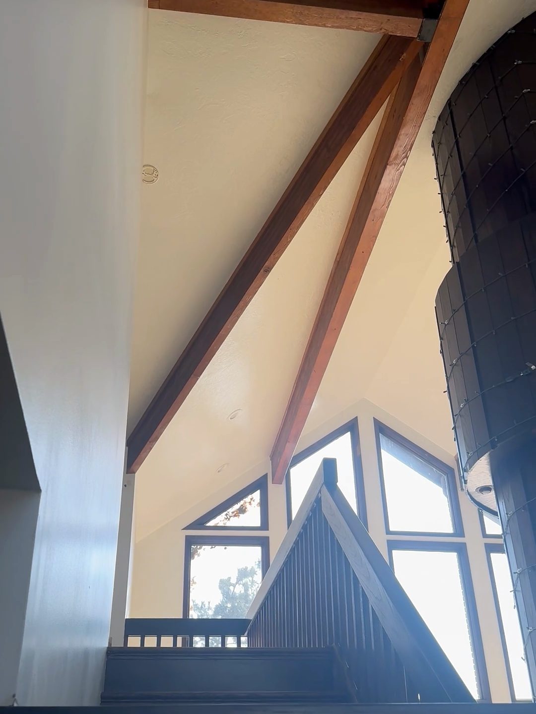 Great room before renovation: exposed beams and angled windows with dark trim