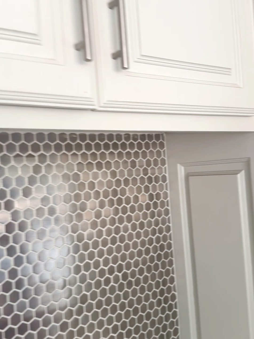 Previous kitchen with white raised-panel cabinets and a steel hex backsplash