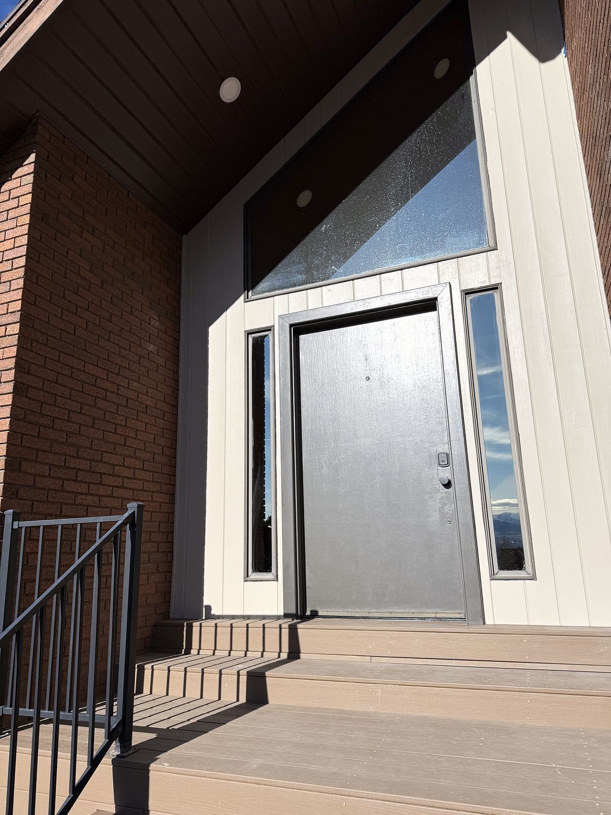 Front entry with brick, pale vertical siding, a steel-gray door and a tall clerestory window