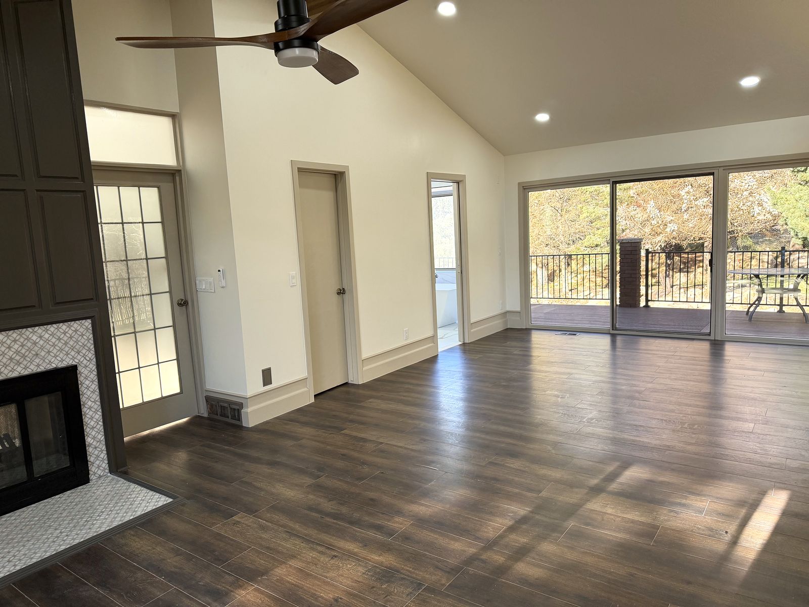 Living room with a vaulted ceiling, dark wood floors, a tiled fireplace and sliding doors to the deck