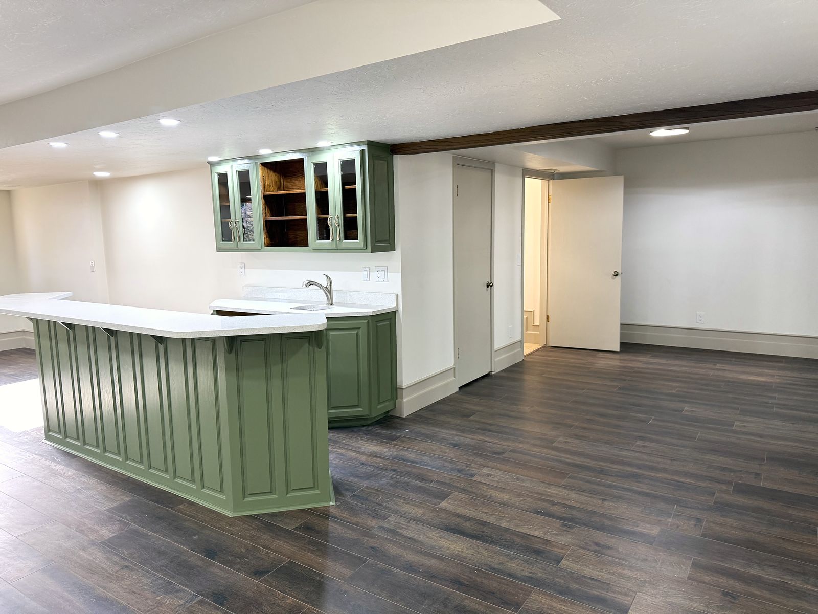 Lower-level bar with sage-green paneled cabinetry and white counters