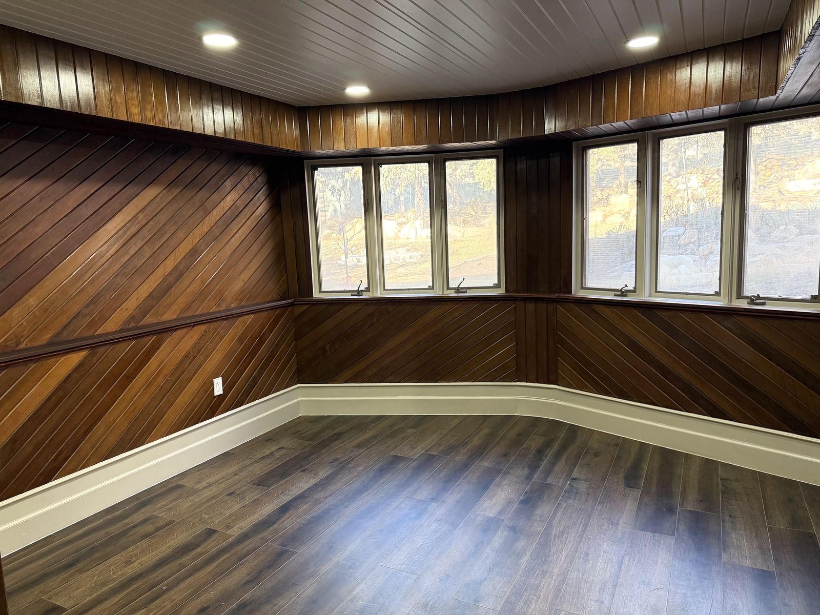 Den wrapped in warm wood paneling with a band of windows