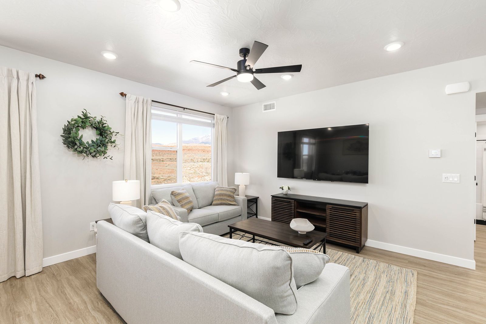 Minimal living room with a soft white sectional, wood coffee table and a window framing red desert hills