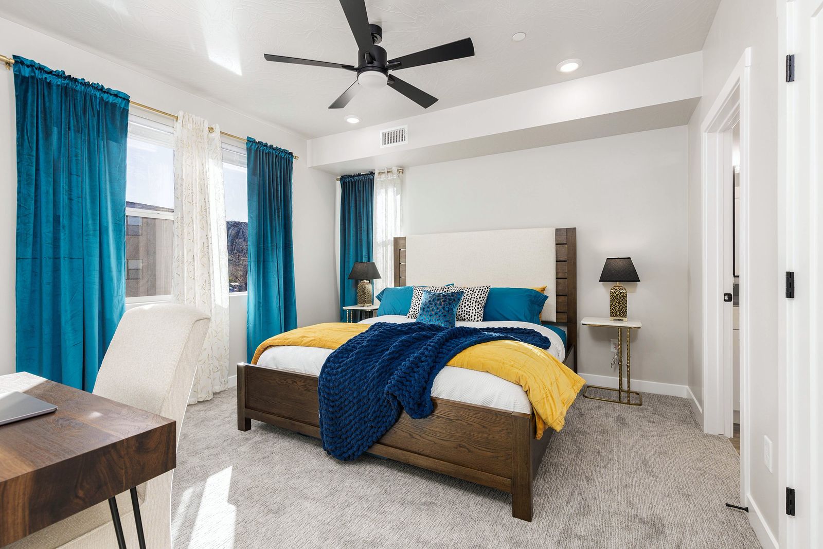 Bedroom with teal curtains, a wood bed, yellow and navy bedding and a writing desk