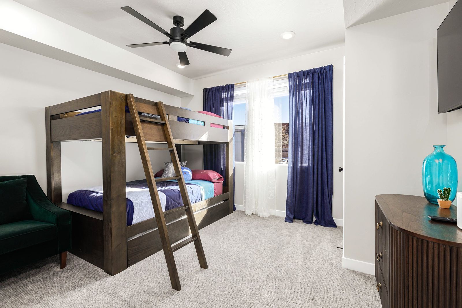 Bunk room with a solid wood bunk bed, navy curtains, a green velvet chair and a teal glass vase