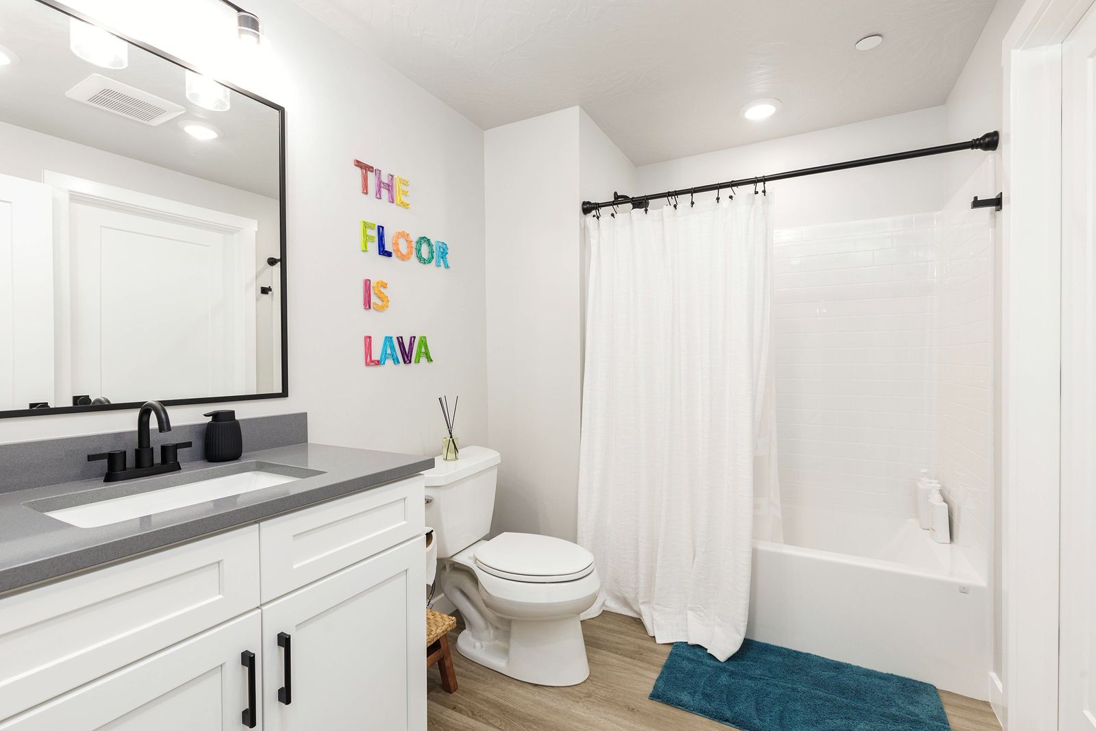 Bathroom with colorful The Floor is Lava wall letters and a teal bath mat