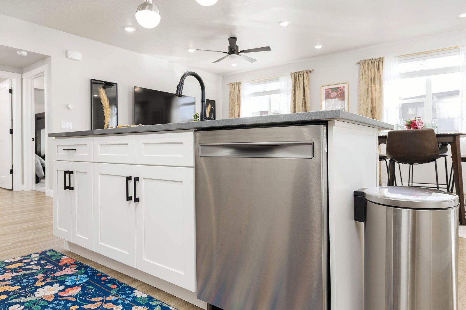 Kitchen island with a dishwasher and bright patterned rug, looking toward the living room