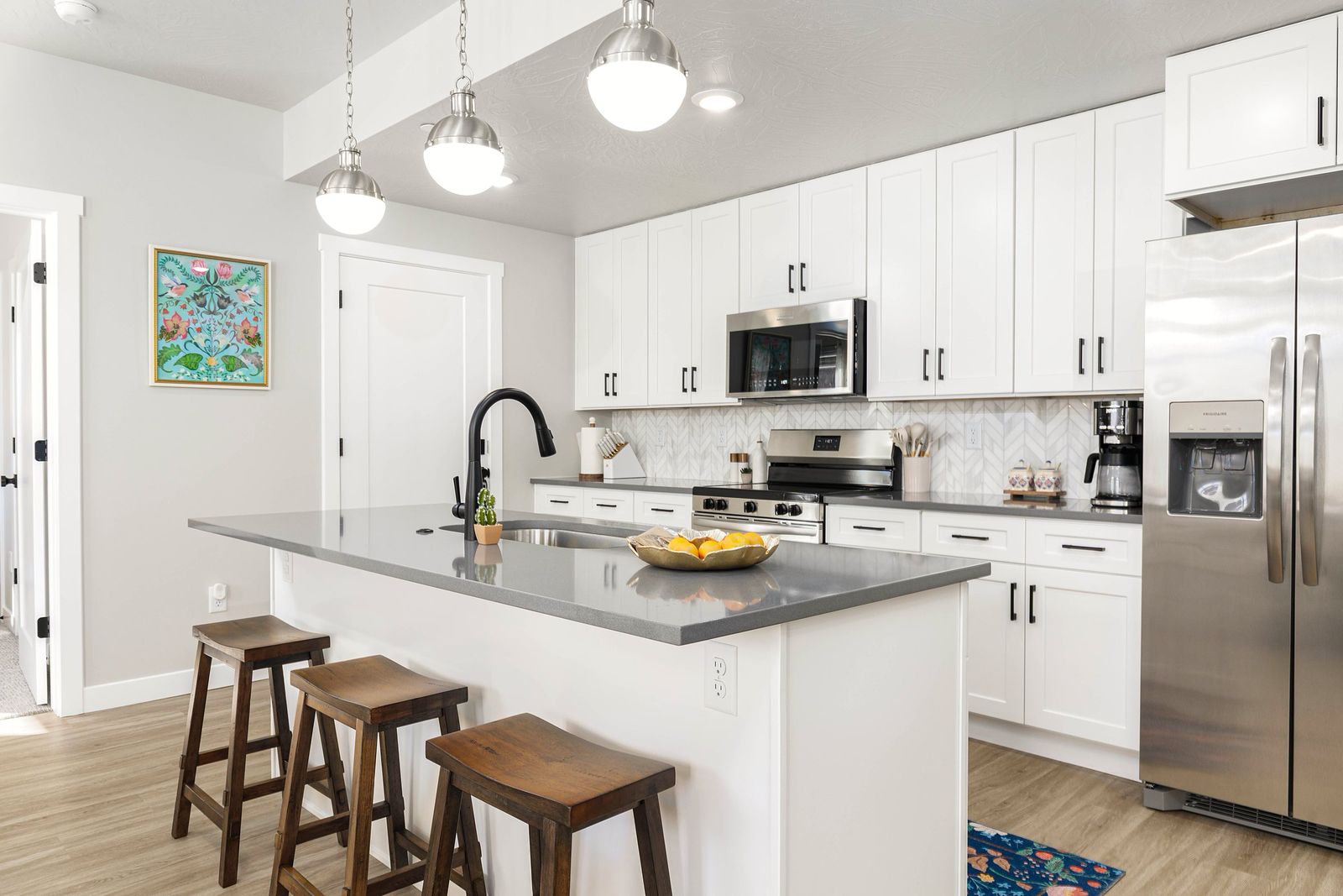 White kitchen with wood counter stools, brass-toned details and colorful art