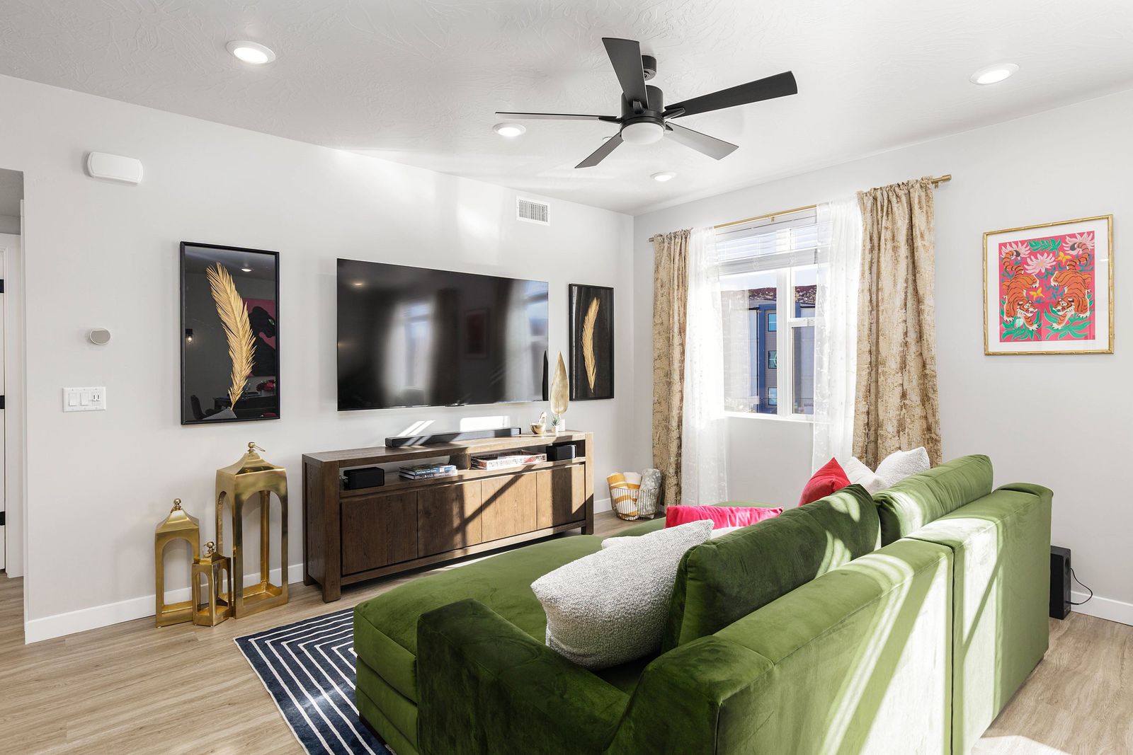 Living room with green velvet sectional, patterned rug, framed art and a warm-wood media console