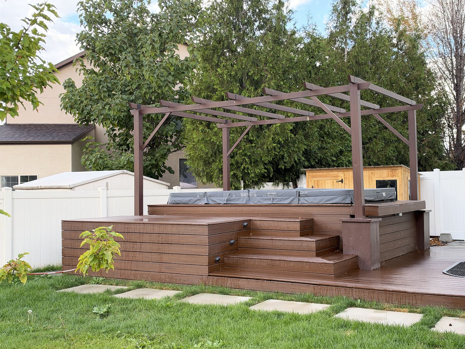 Tiered stained-wood deck with wide built-in steps, a covered hot tub and a pergola, stepping pads across the lawn