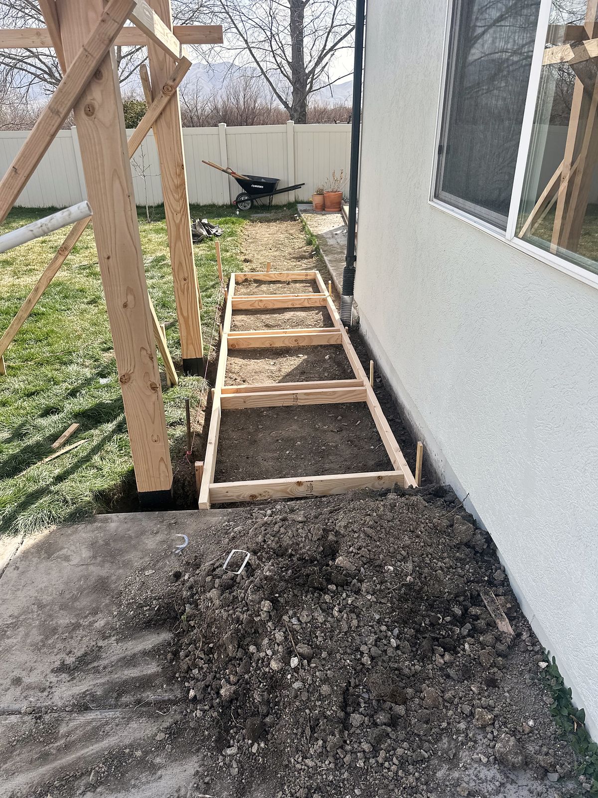 New pergola posts braced beside a narrow raised bed along the house